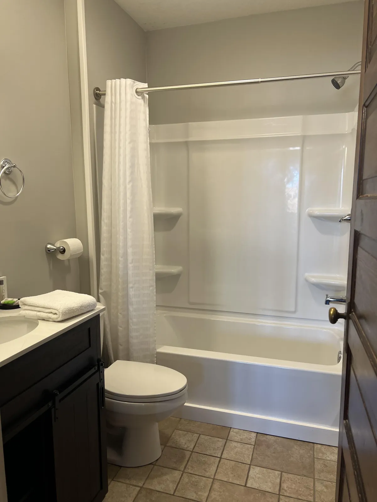 A modern, tidy bathroom with a white shower curtain, dark cabinetry under the sink, a toilet, and a tiled floor. The space is uncluttered and bright, evoking a sense of calm and cleanliness.