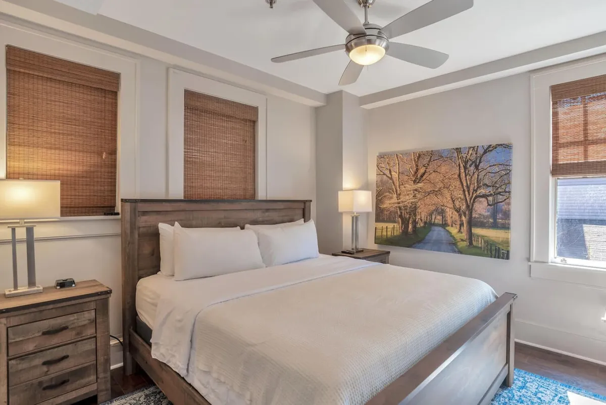 A serene bedroom with a large, inviting bed framed by elegant nightstands and lamps, along with tasteful artwork above the headboard. The atmosphere is peaceful, highlighted by gentle natural light.