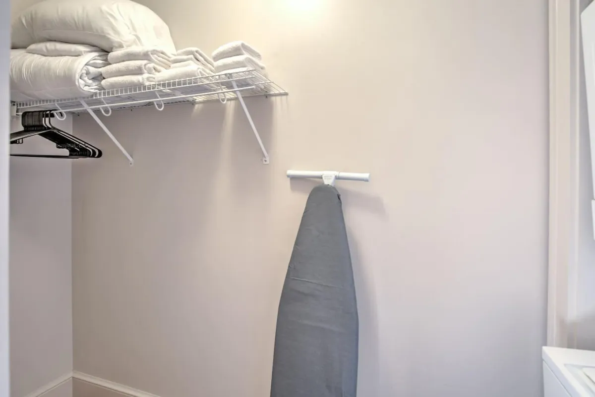 A practical utility nook featuring shelves stacked with towels, hanging clothes, and an ironing board, all neatly arranged to hint at organization and readiness for city living.
