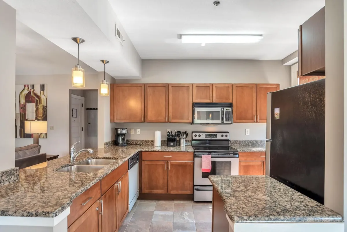 This image showcases a modern kitchen featuring granite countertops, stainless steel appliances, and warm wooden cabinets. Pendant lighting adds both style and function, while the layout is visibly efficient and space-saving. The countertop is clear, suggesting ample workspace for meal preparation.