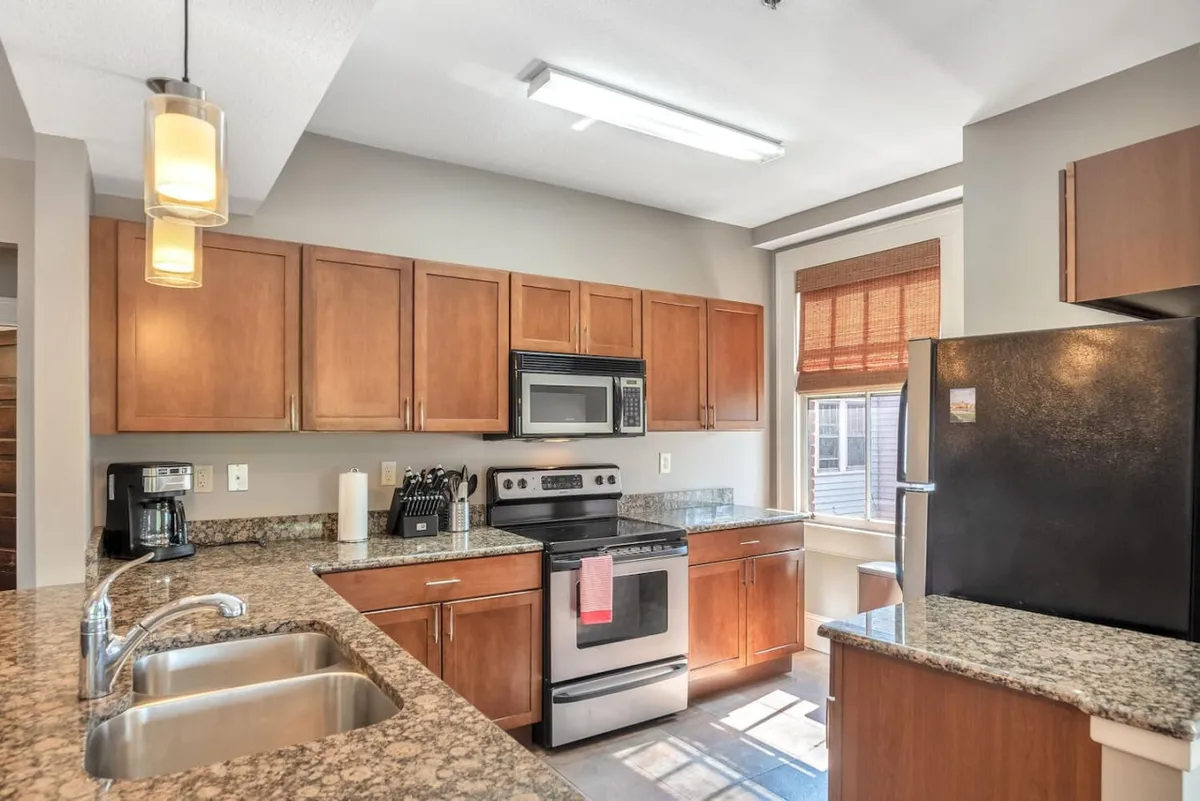 A cozy kitchen scene with a granite countertop, stainless steel appliances, and wooden cabinets. A window lets in natural light, illuminating the workspace and creating an inviting ambiance for cooking or enjoying a morning coffee.